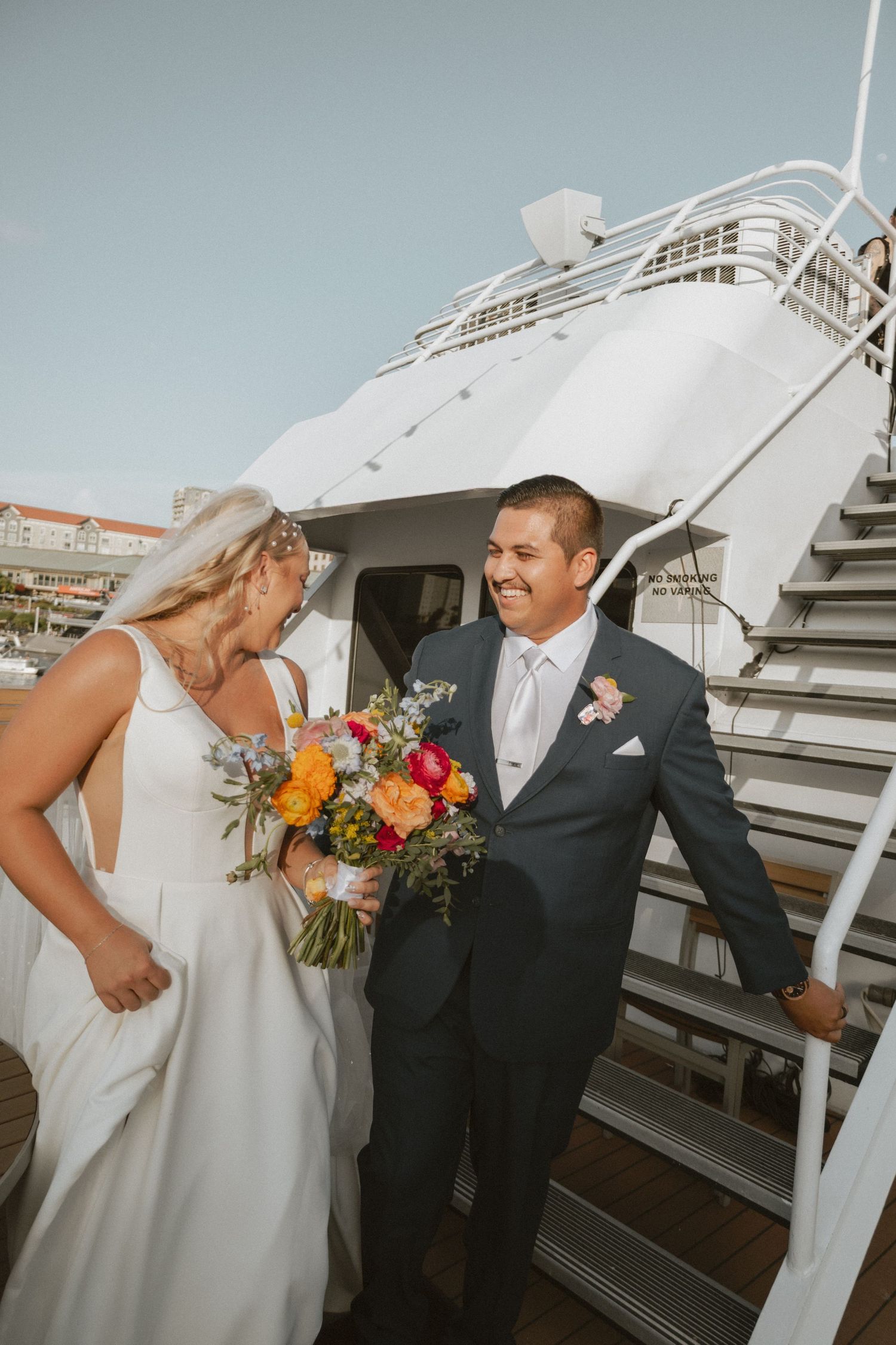A joyful wedding moment captured on a boat deck with colorful bouquet and nautical backdrop.