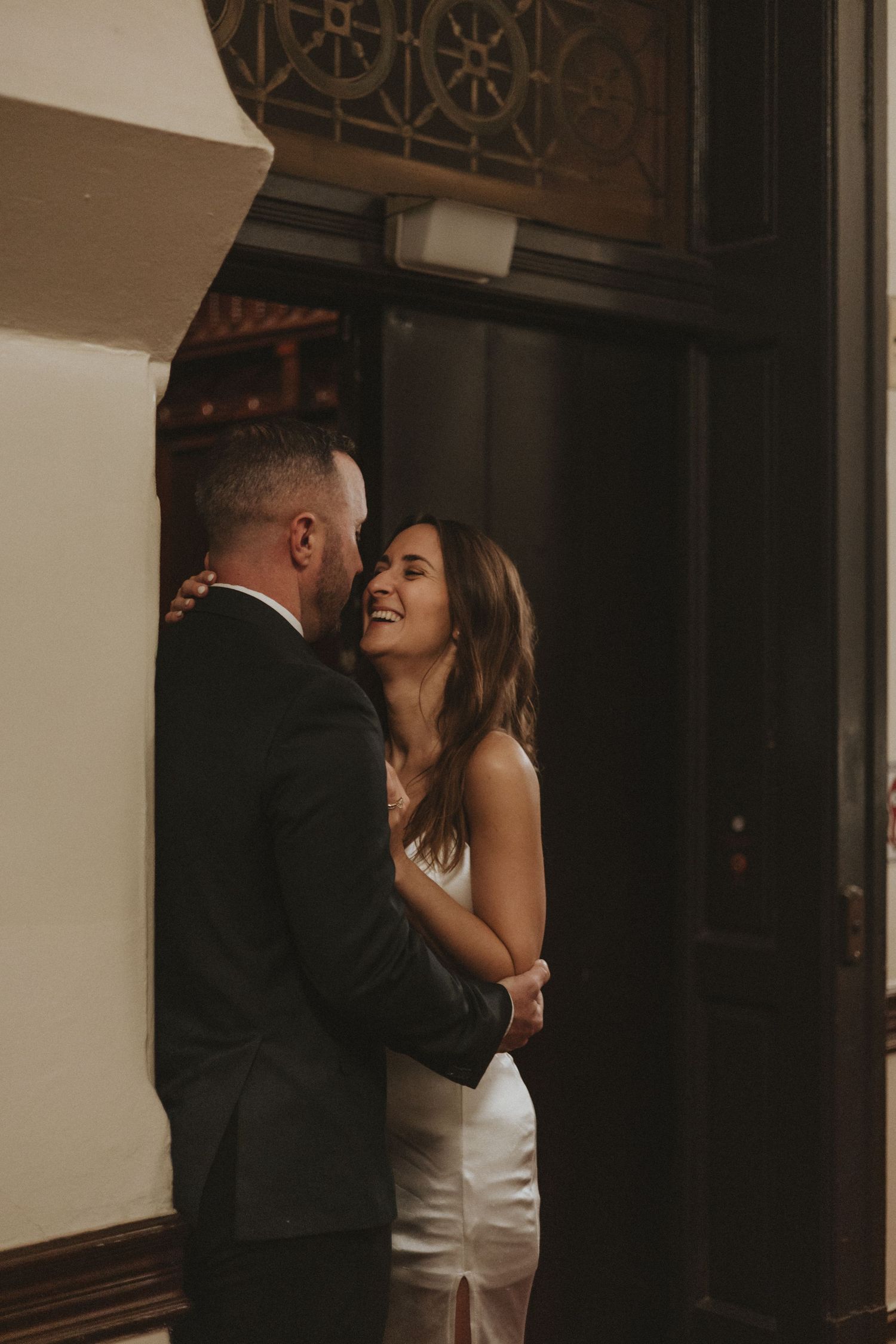 Intimate moment between couple sharing laughter in a dimly lit hallway.