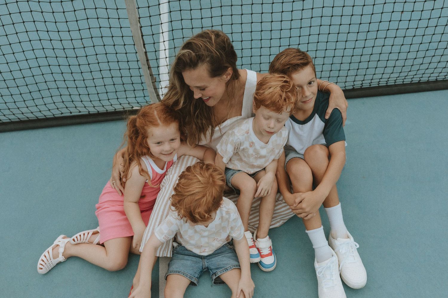 Group of young friends sitting together on a tennis court with a net visible in the background.