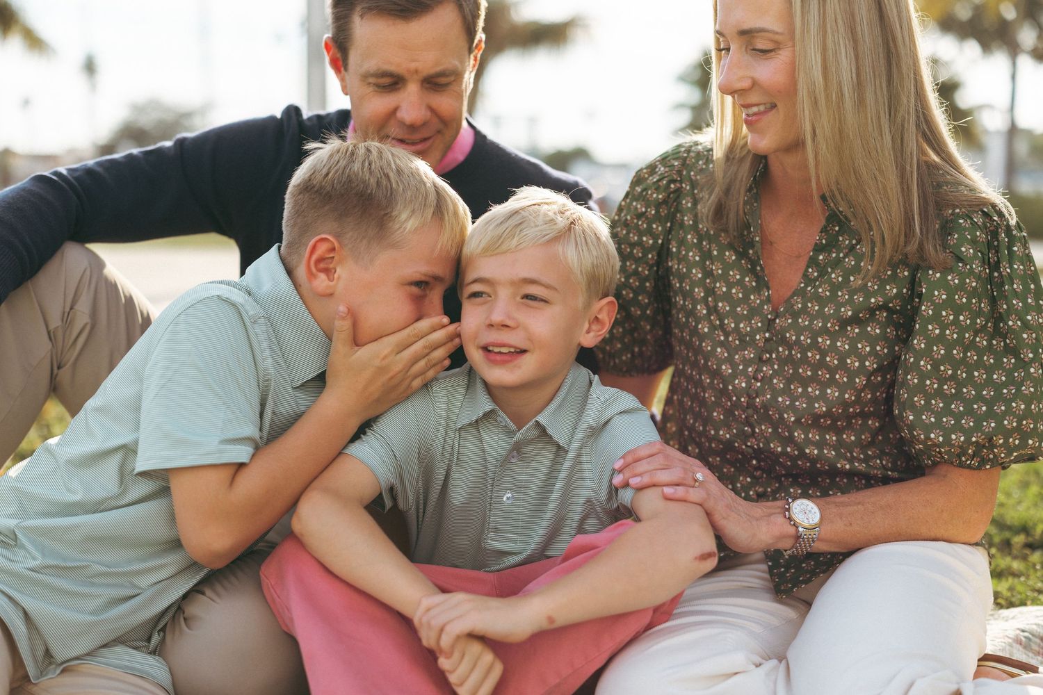 A joyful family relaxes together outdoors while sharing warm embraces and smiles during a sunny day photo session.