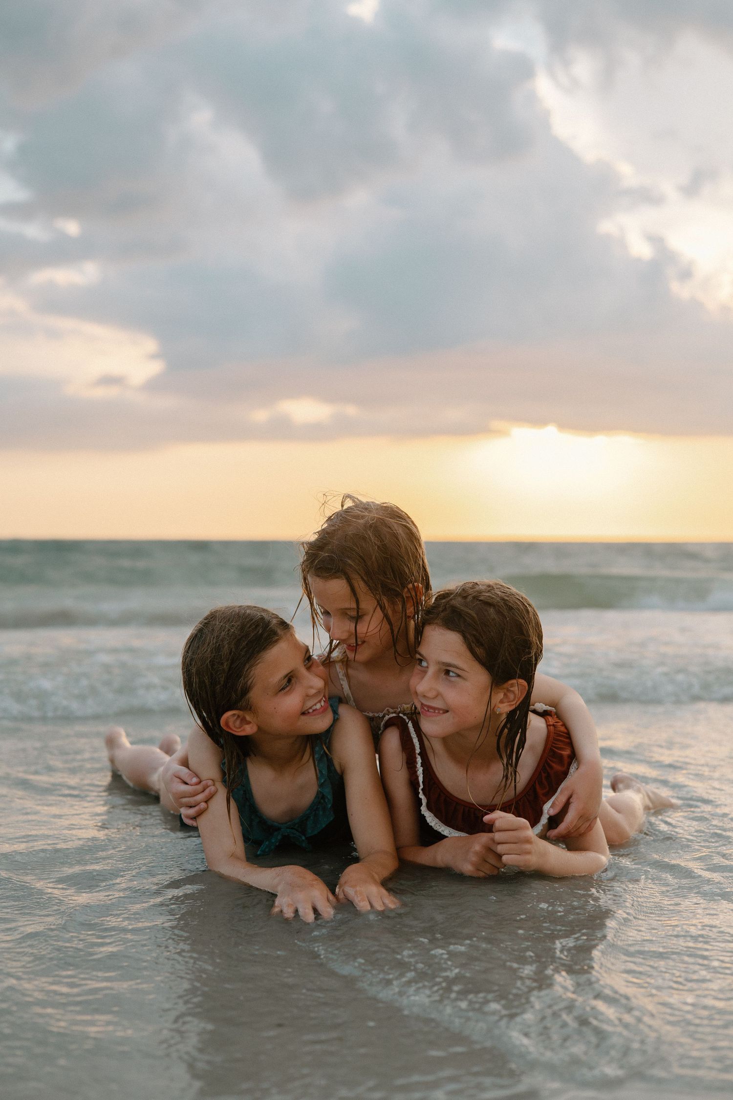 Three people lying together playfully in ocean waves at sunset.