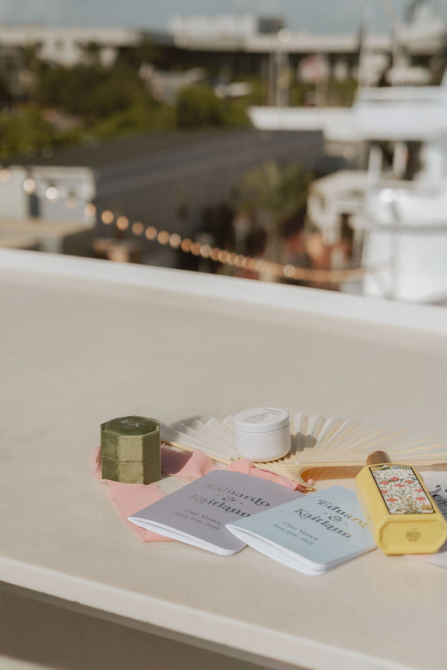 Wedding details including small notebooks and decor items on a white surface with string lights in background.