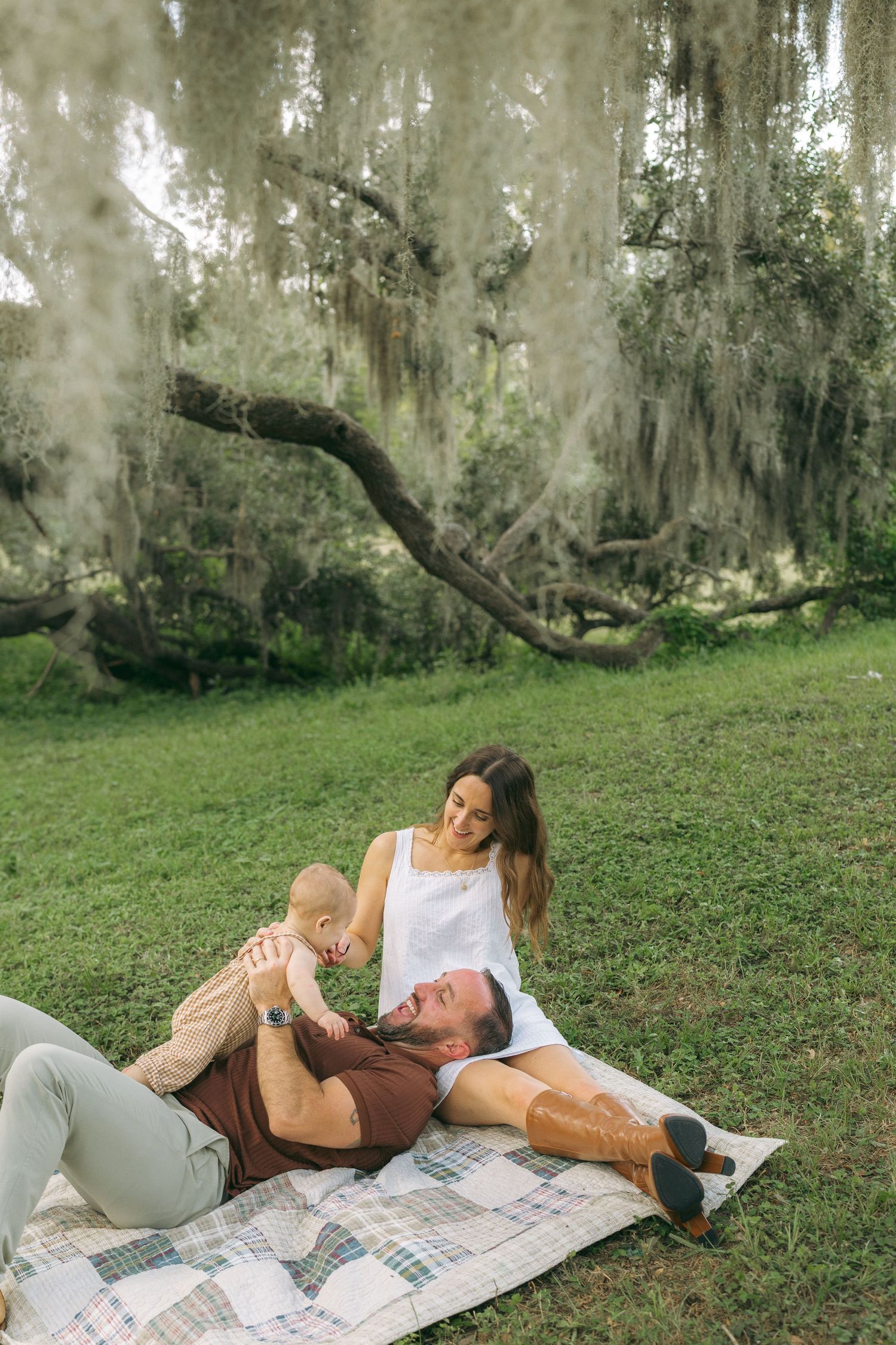 Family enjoying a picnic on a blanket under Spanish moss-draped trees in a lush green park.