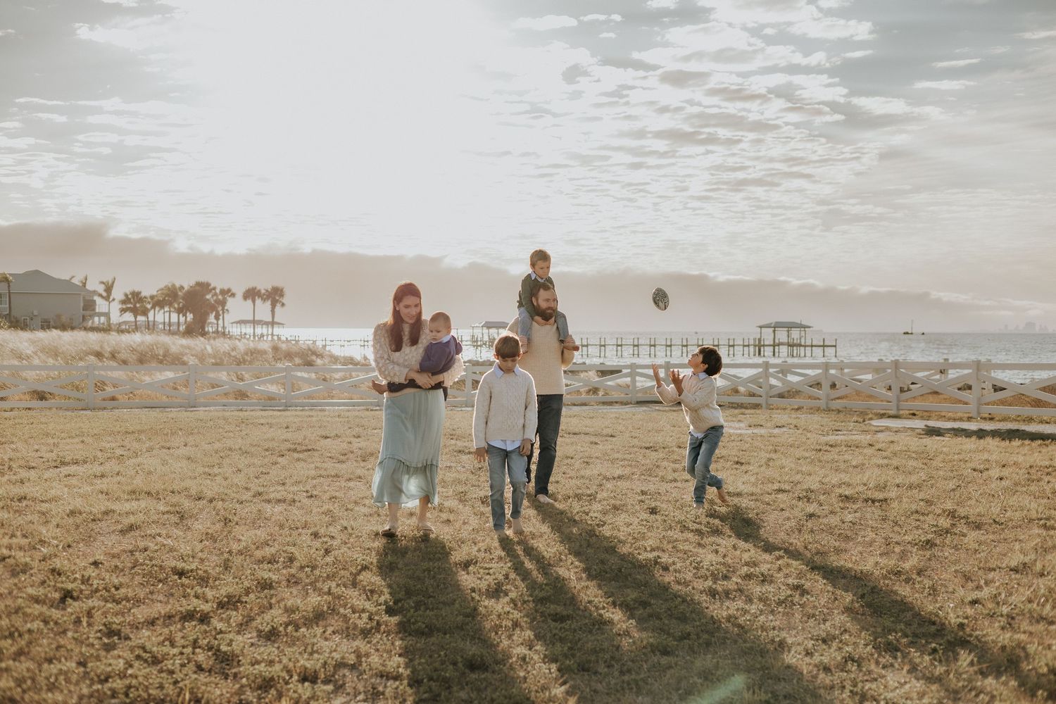 Family silhouettes walking together across a sunlit field at sunset.