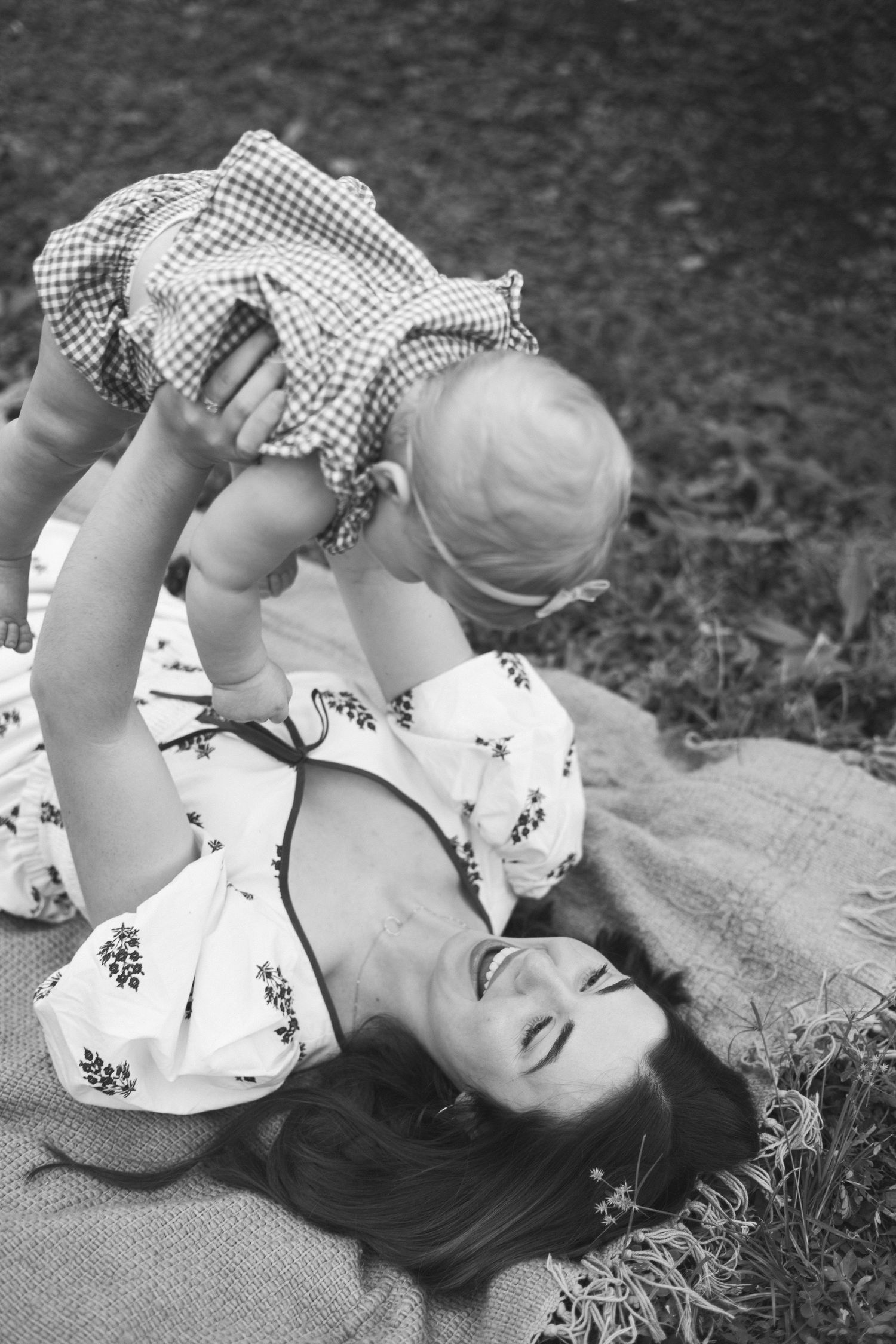 A black and white photograph showing a tender moment of play between parent and child on a blanket outdoors.