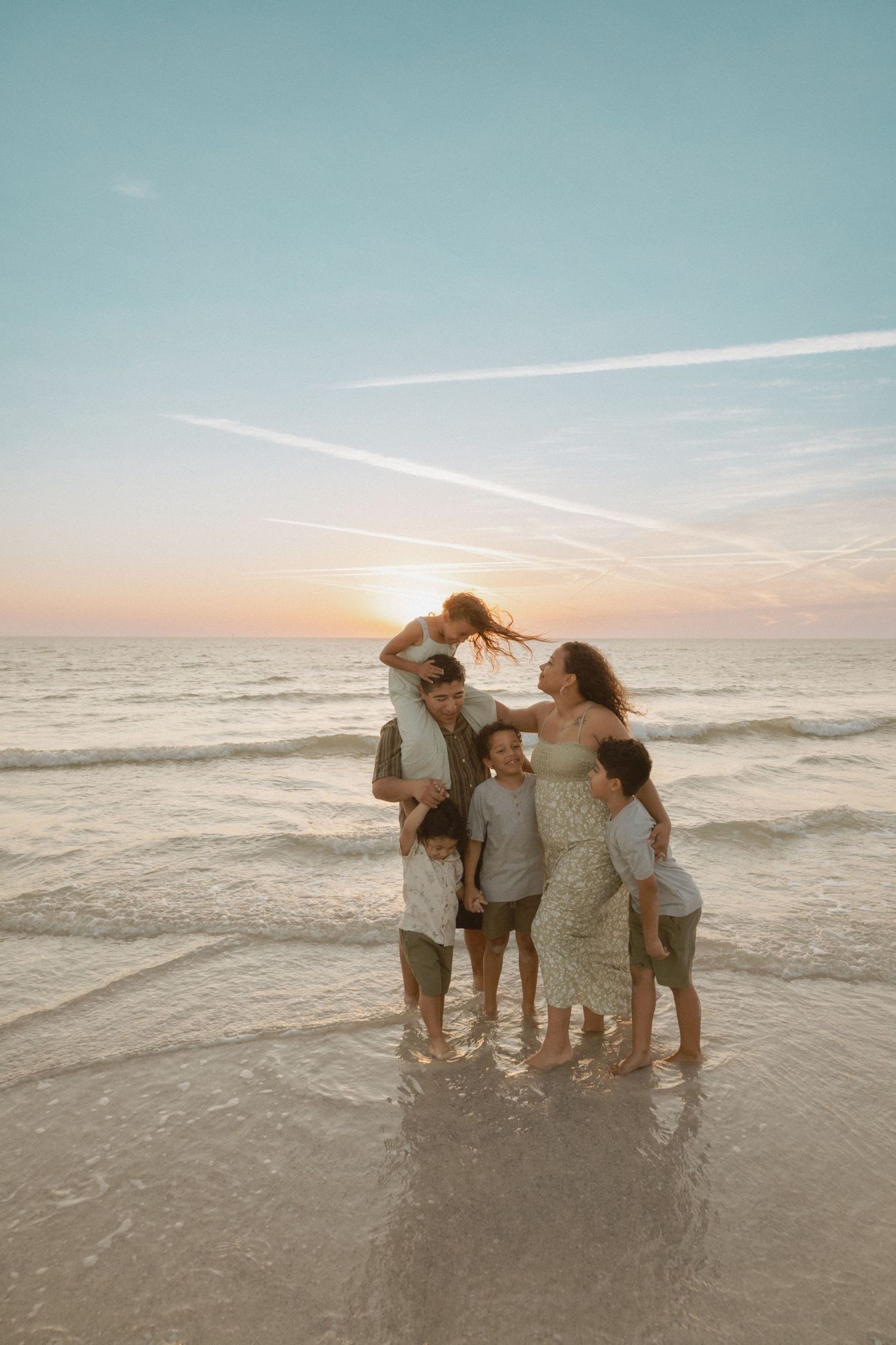 Family sharing intimate moment together in ocean waves during sunset.