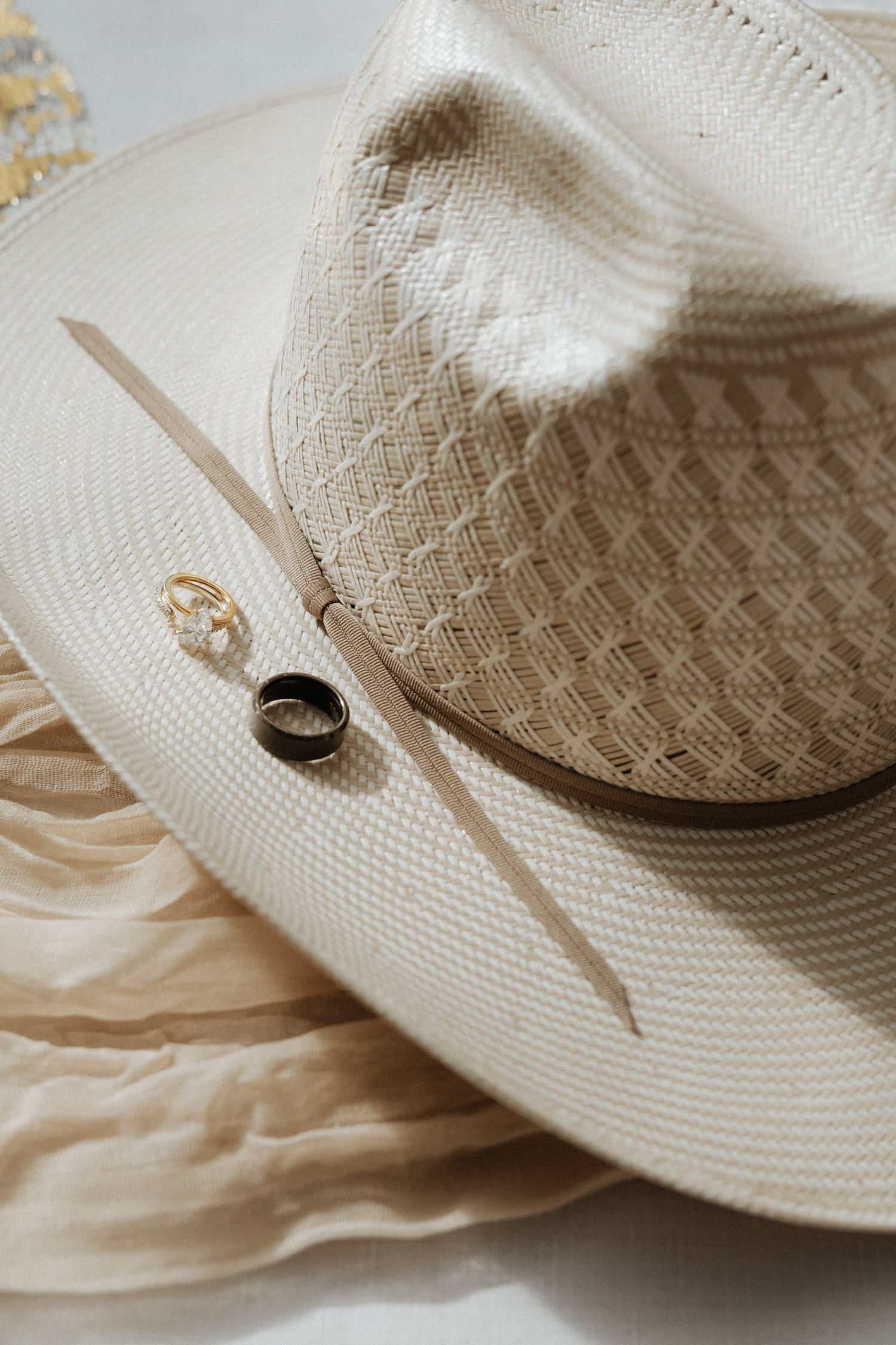 Vintage white cowboy hat with wedding rings placed on its brim.