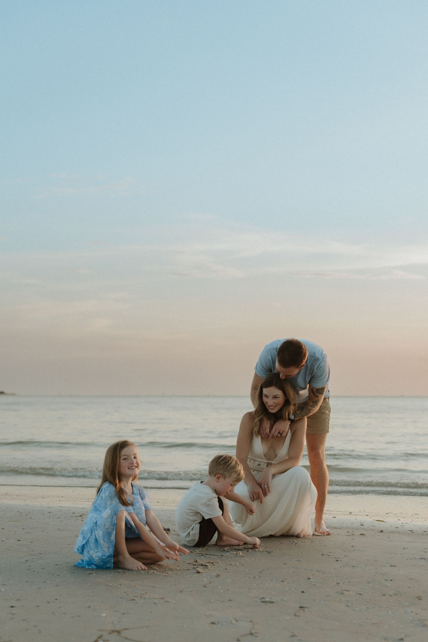Family of four enjoying a peaceful beach sunset, with children playing in the sand while parents share a tender moment.