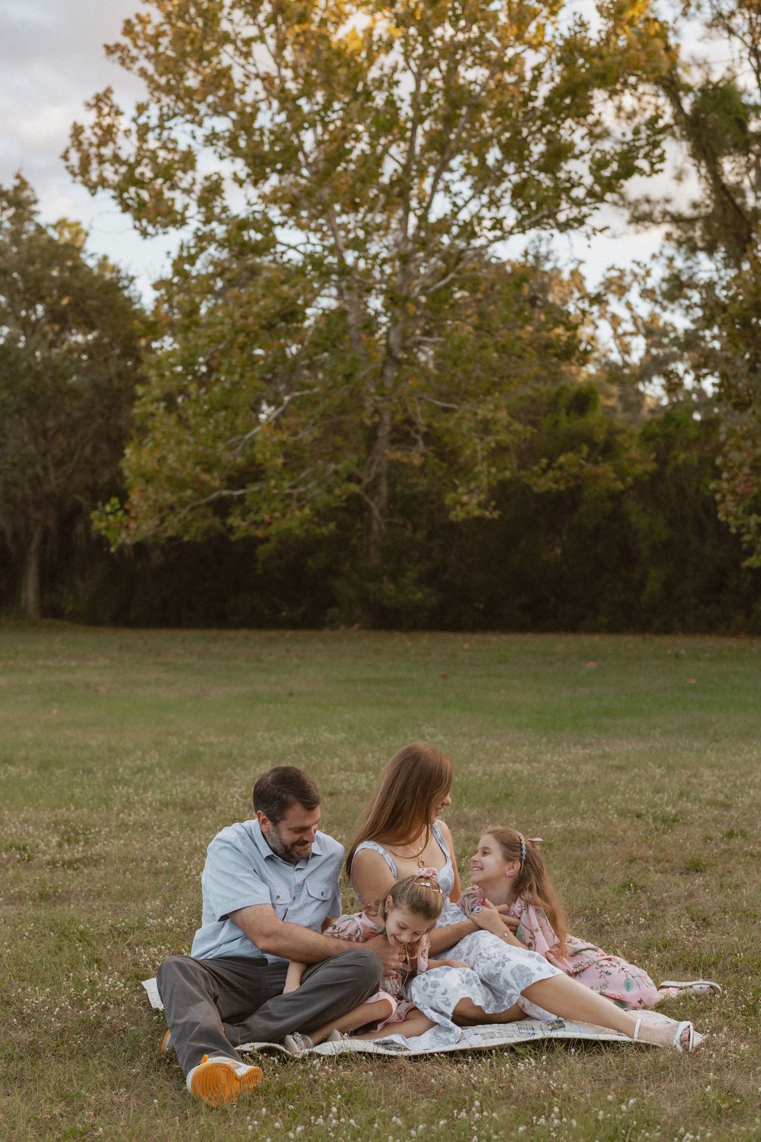 Family relaxing together on a picnic blanket in a grassy field during golden hour.