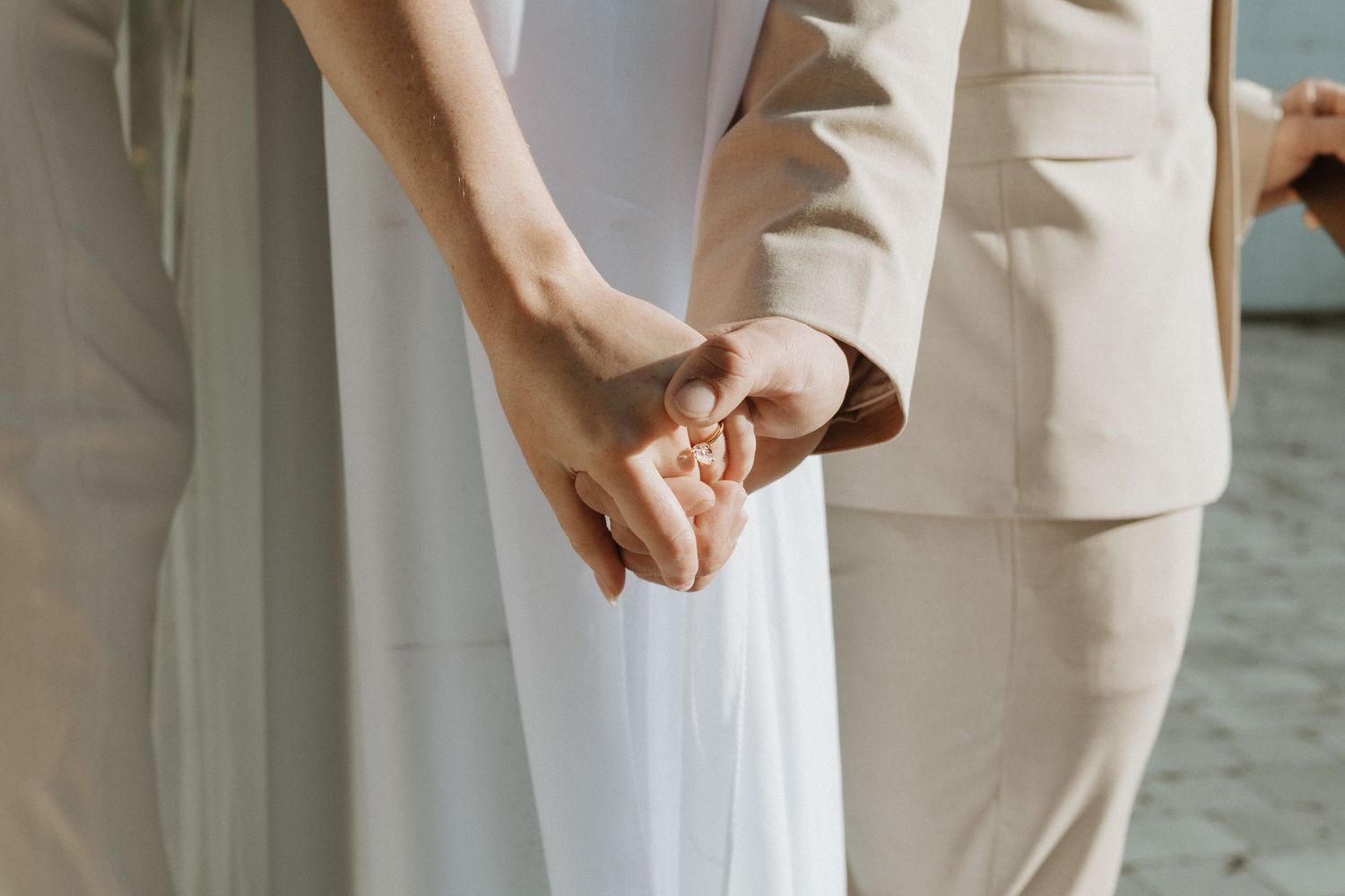 Two hands gently touching fabric details on a light colored formal outfit.