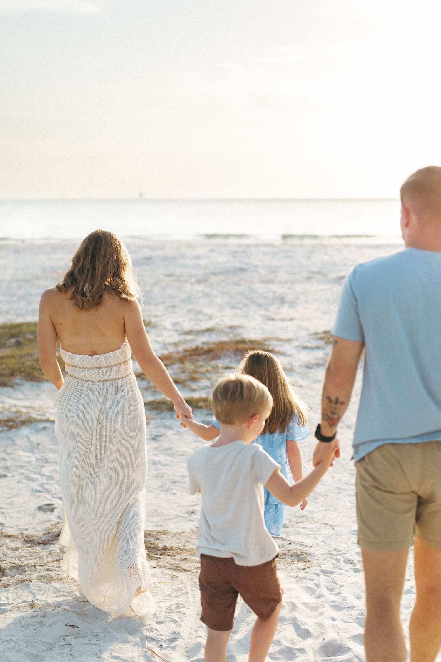 Family of four walking hand-in-hand toward the ocean on a sunny beach day.