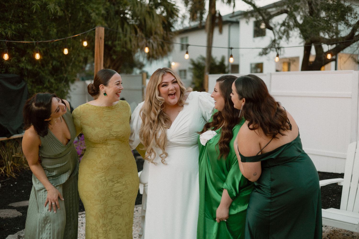 A group shares laughter and embraces during a wedding celebration outdoors with string lights.