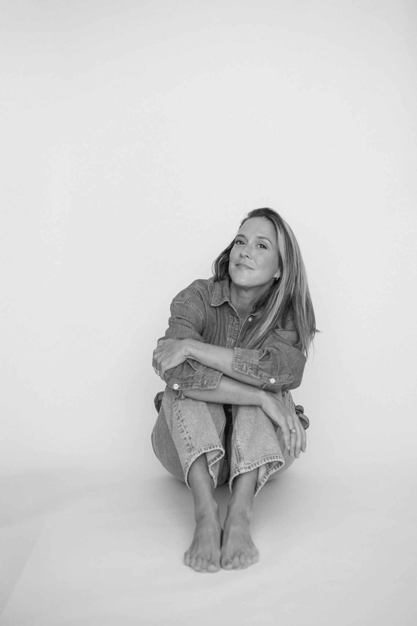 Black and white photo series showing a person in casual denim clothing sitting in various relaxed poses against a white backdrop.