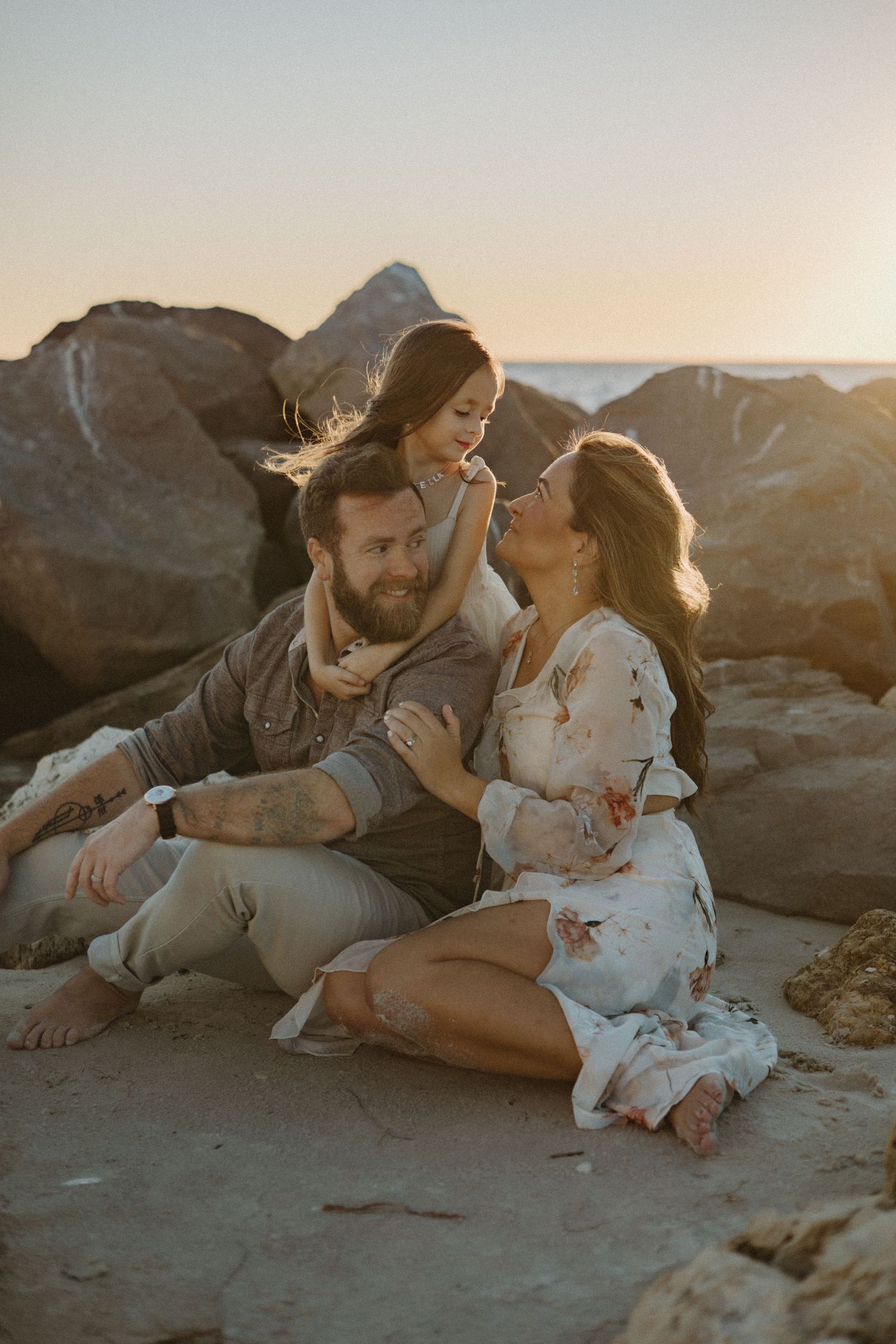 Intimate family moment on rocky beach during golden hour.