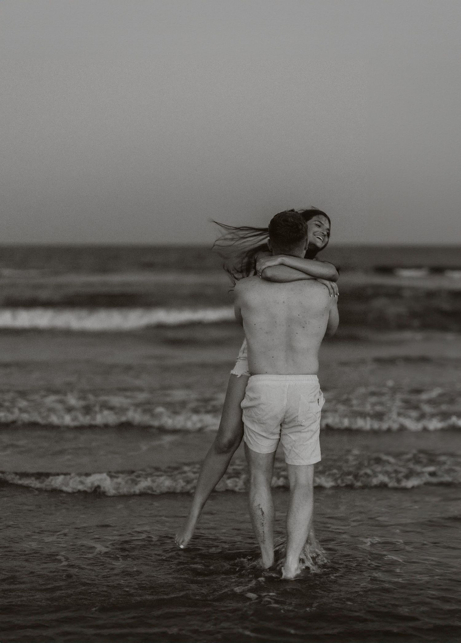 Artistic black and white sequence of a couple playing in ocean waves at the beach.