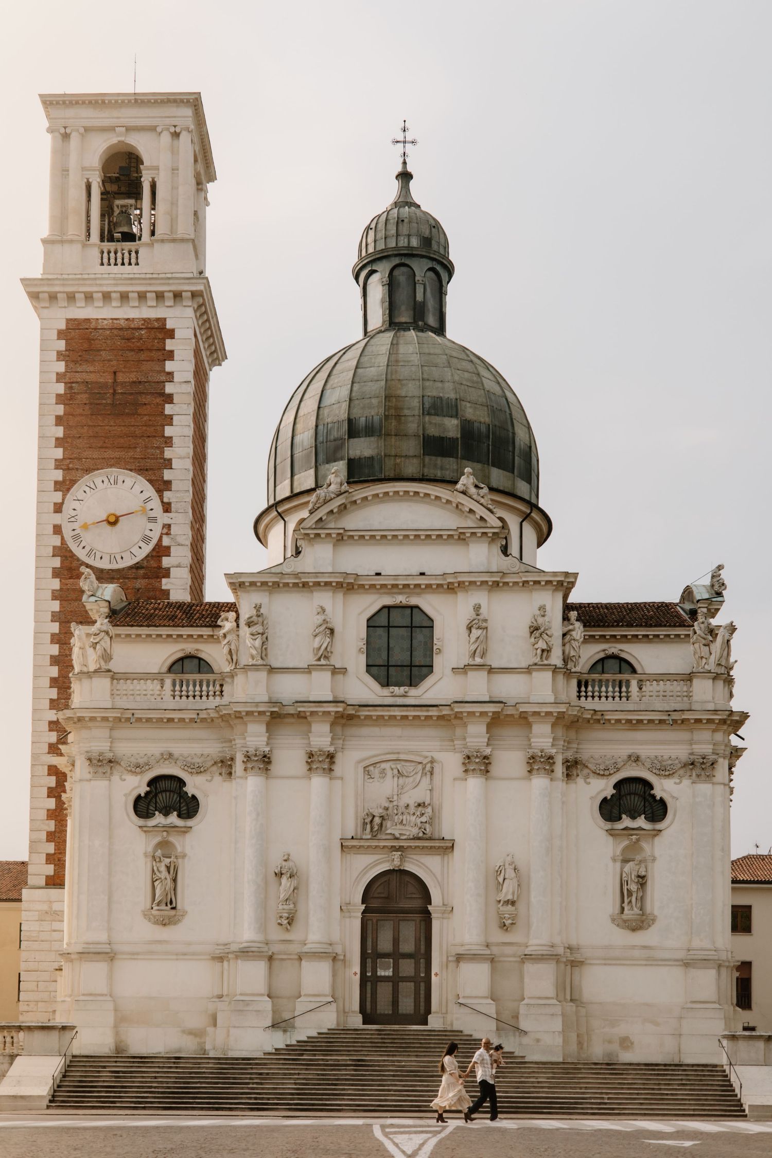Majestic white church with domed roof and brick bell tower against cloudy sky.