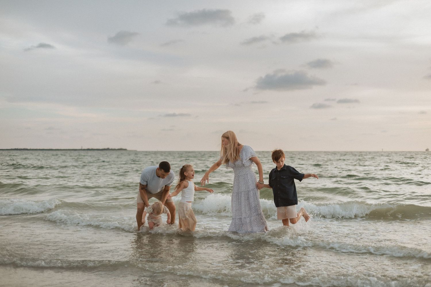 Wedding party splashing and playing in ocean waves at sunset beach celebration.