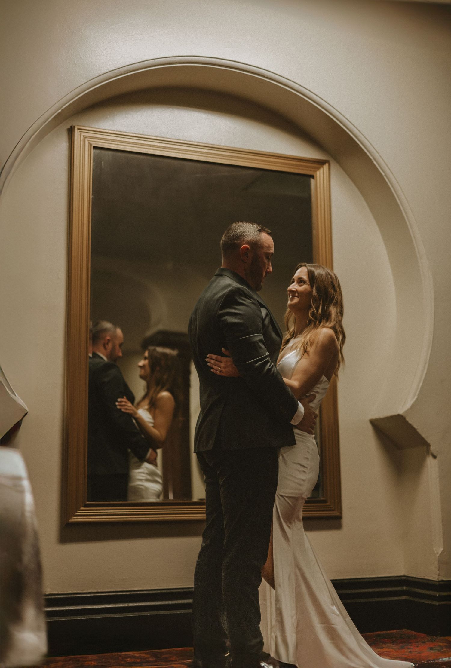 Wedding couple dancing in front of ornate mirrors in an elegant indoor setting.