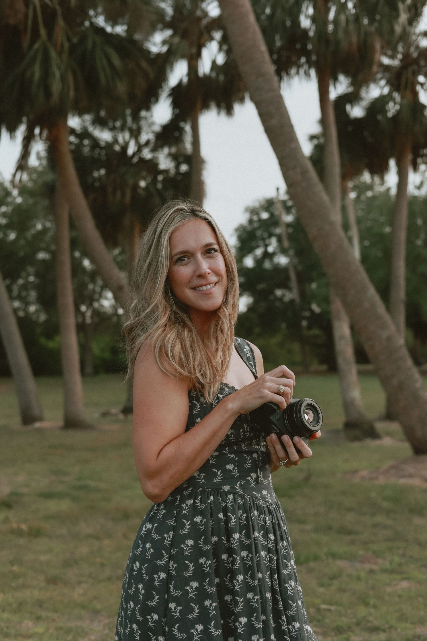 A person in a green floral dress poses playfully in a series of four outdoor photos among palm trees.