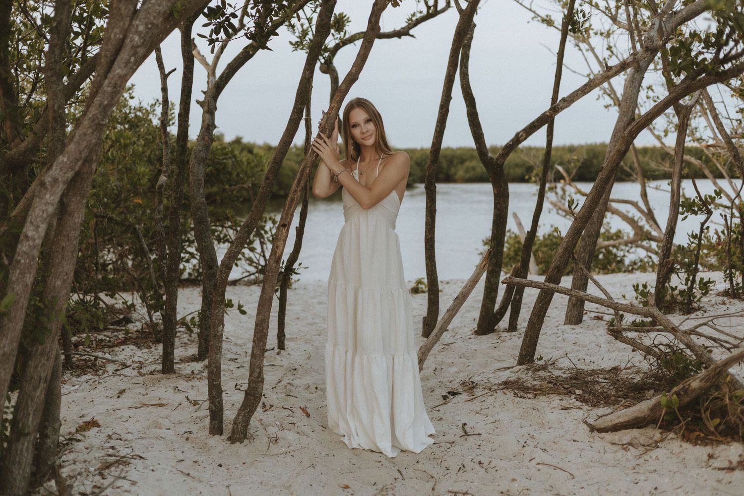 Series of ethereal beach photos with white dresses among natural coastal trees.
