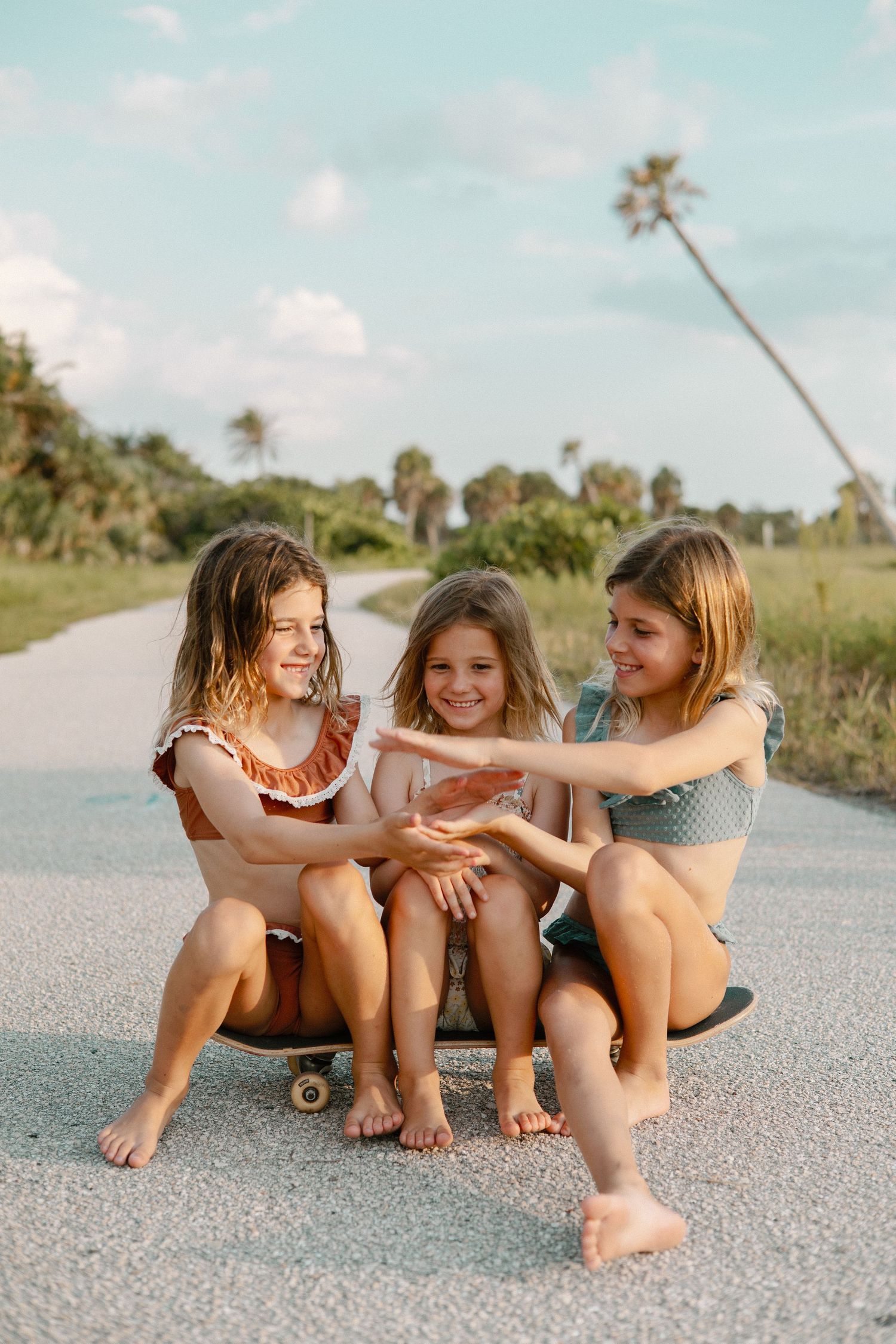 Three friends sitting and laughing together on a beach path on a sunny day.