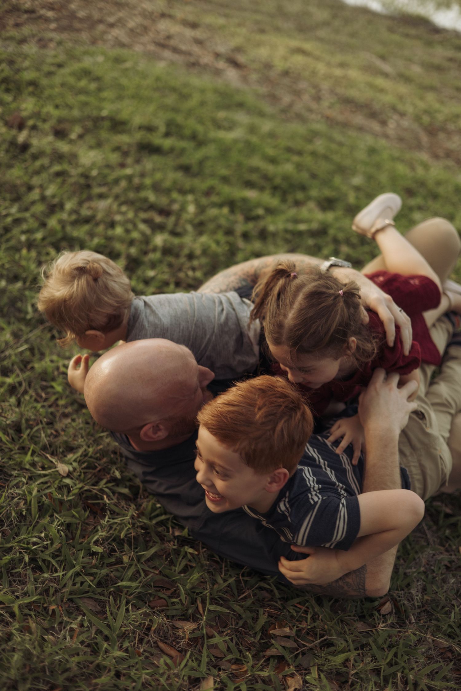 Playful family pile on grassy hill sharing intimate moment together.
