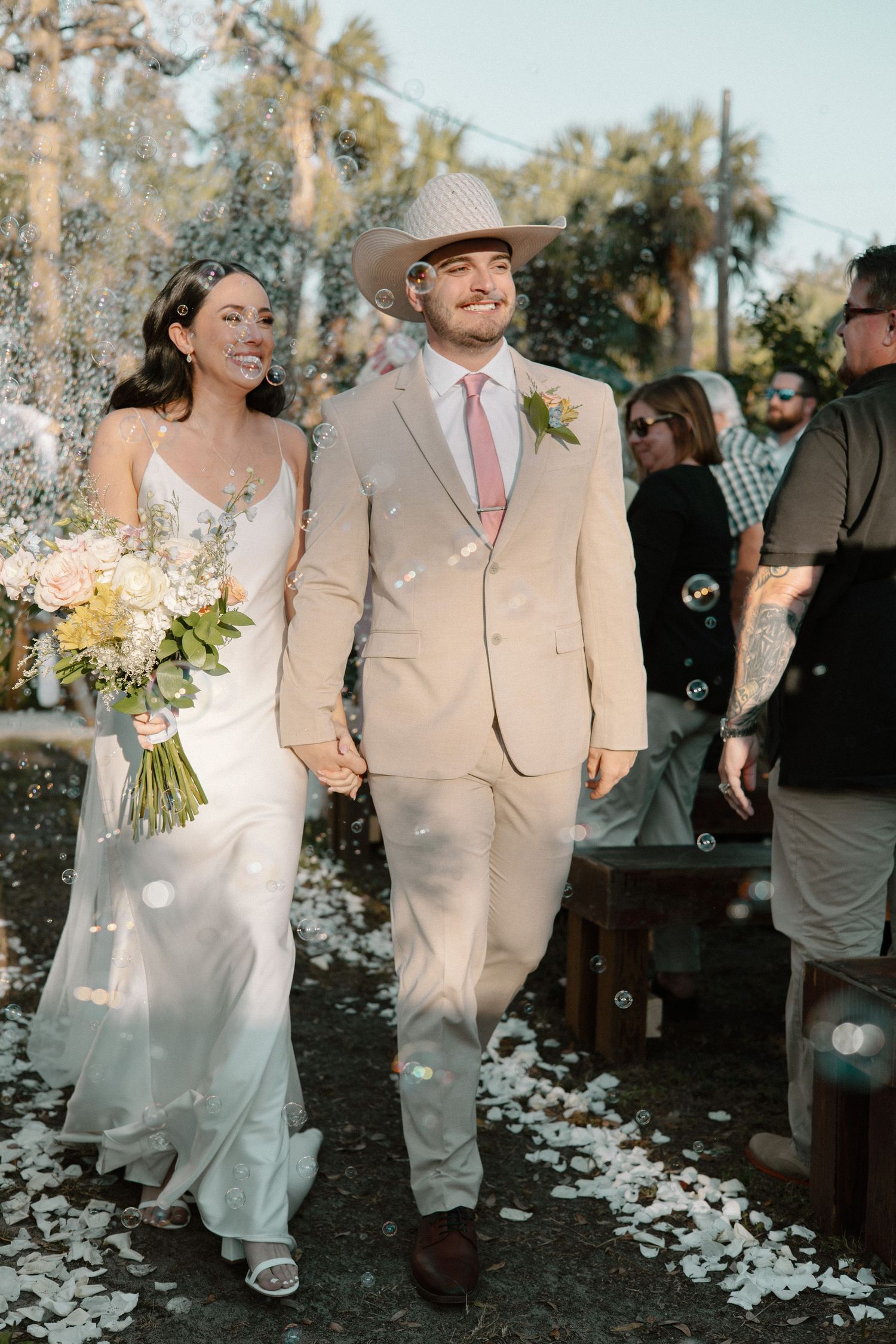 Wedding ceremony guests throwing white flower petals during an outdoor celebration.