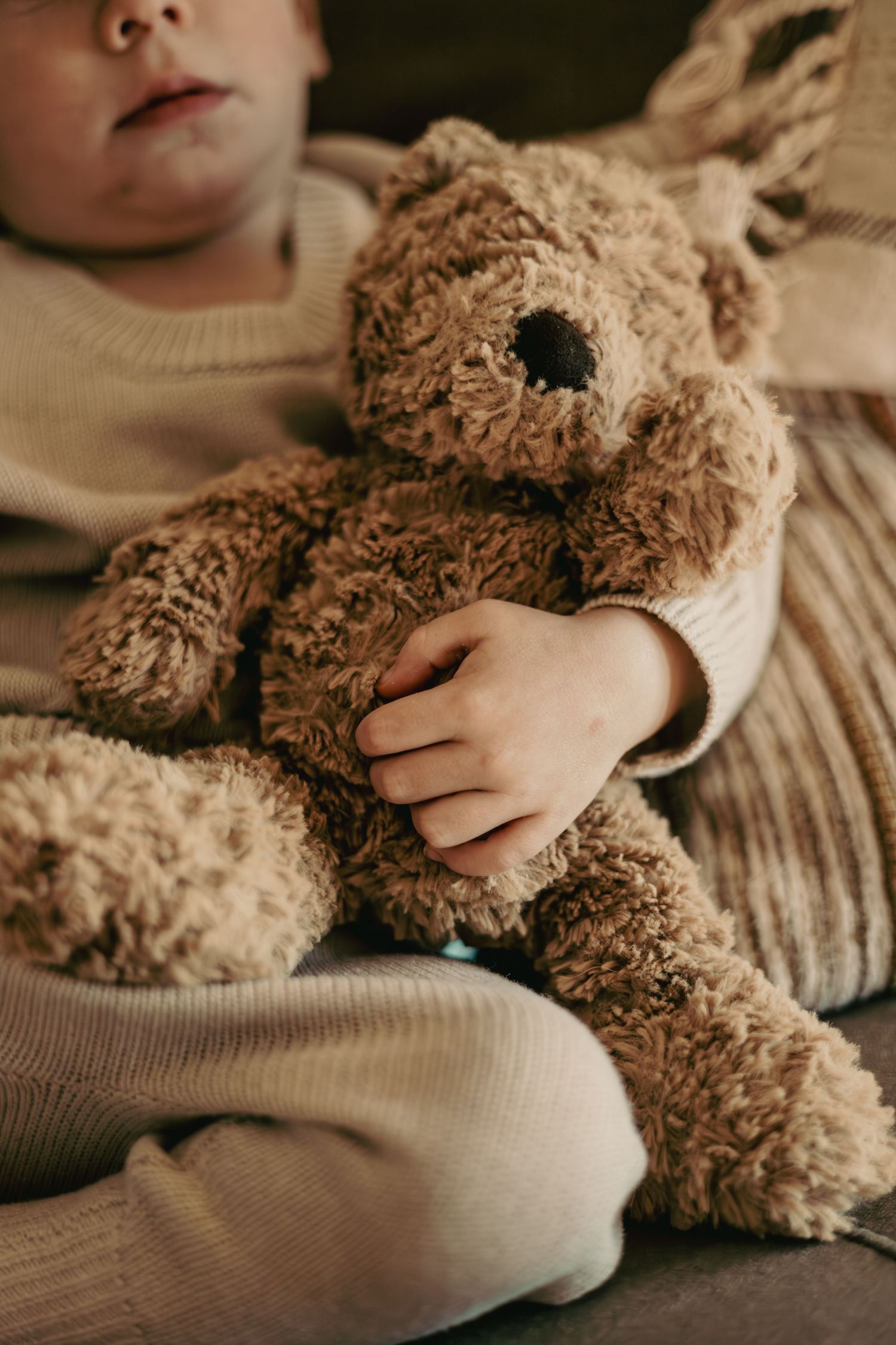 Close-up series of teddy bear being cuddled by someone wearing a beige sweater in warm sepia tones.