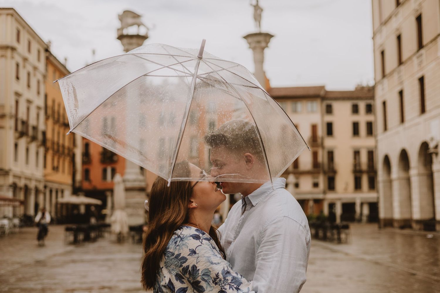 Romantic sequence in a historic Italian plaza with umbrellas on an overcast day.