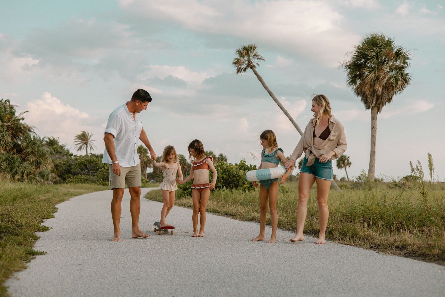 Family group walking together along palm-lined beach path.