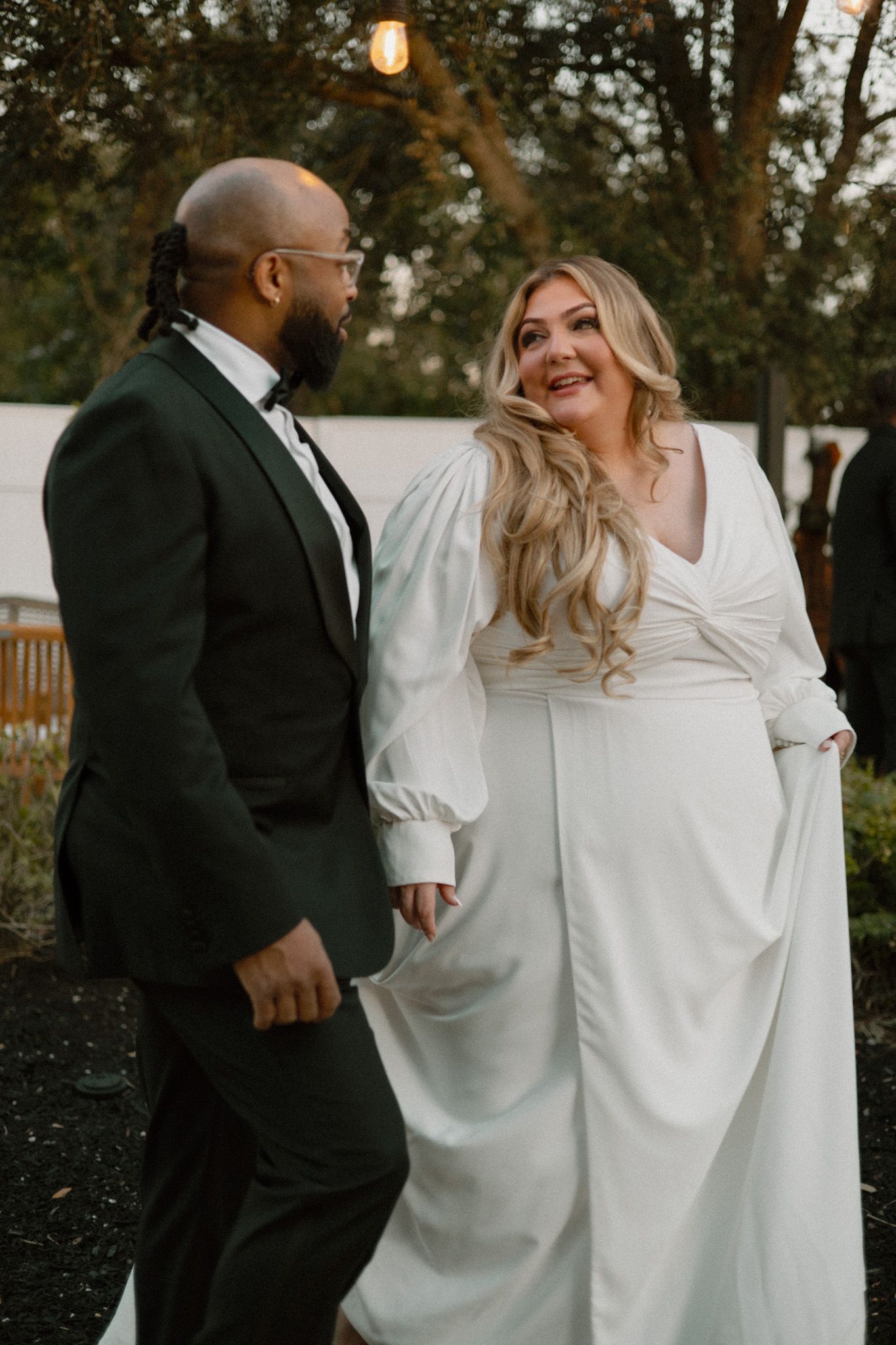 A couple in formal wedding attire sharing a joyful moment during their outdoor celebration.