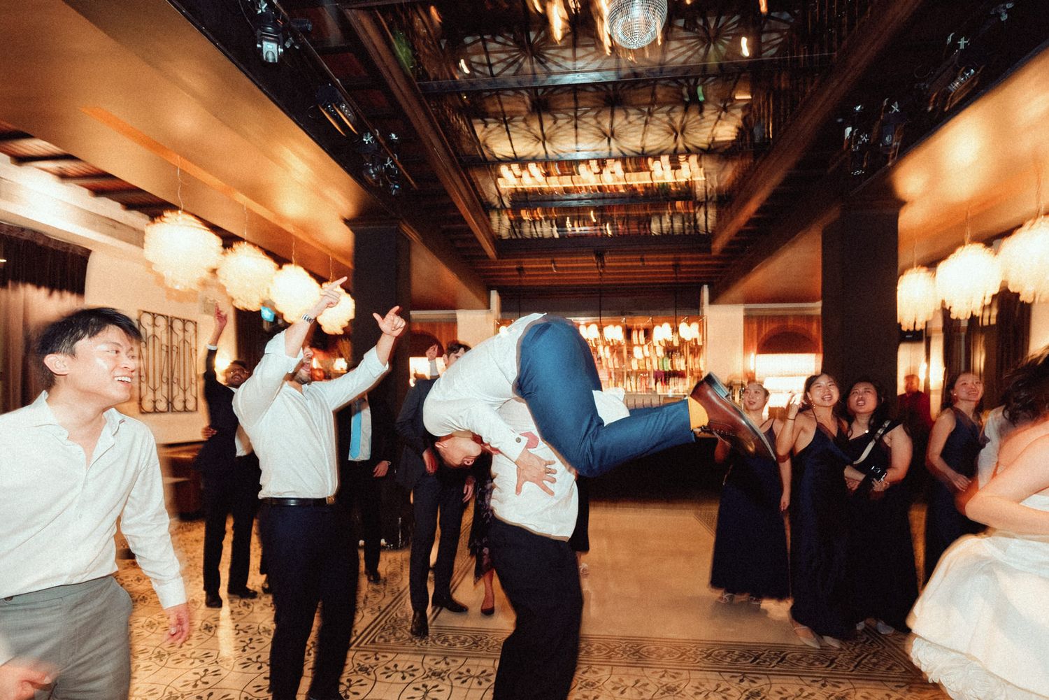 Couples dance together at a wedding reception in a warmly lit indoor venue with rustic wooden beams and string lights.