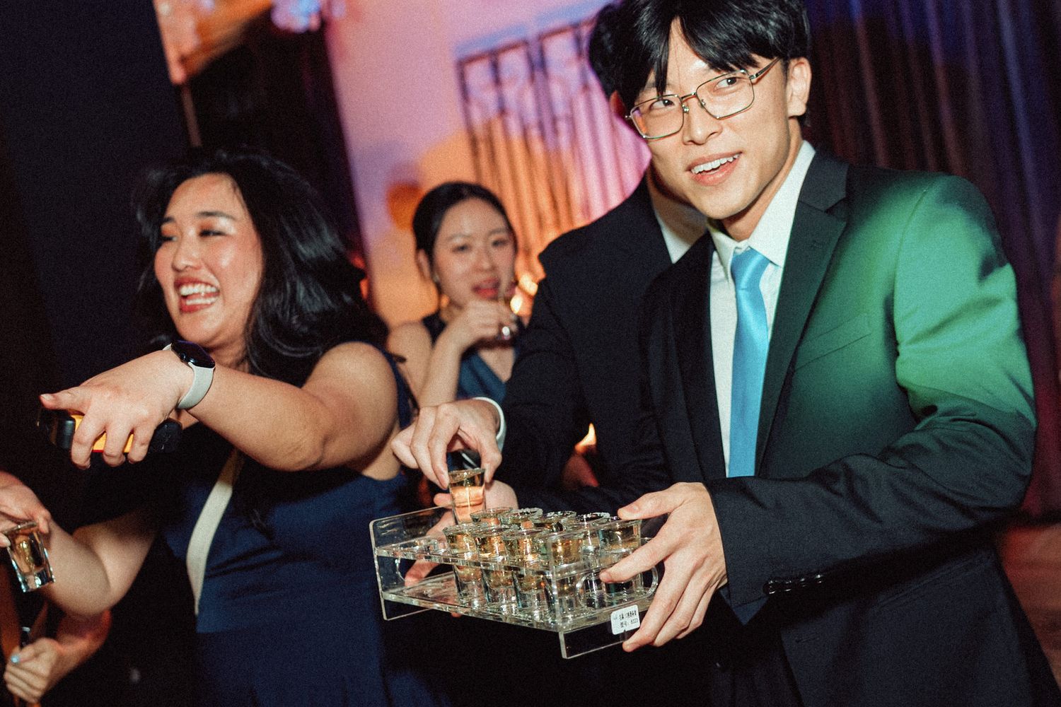 Guests at an elegant event enjoy drinks and conversation in a dimly lit venue with turquoise and green accents.