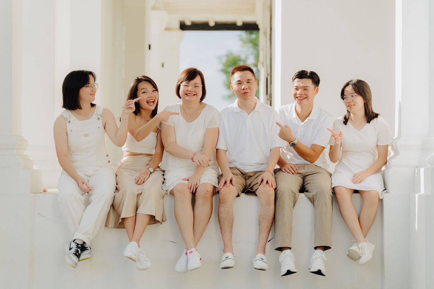 A group of bridesmaids in white dresses sit together laughing and sharing a joyful moment at a wedding celebration.