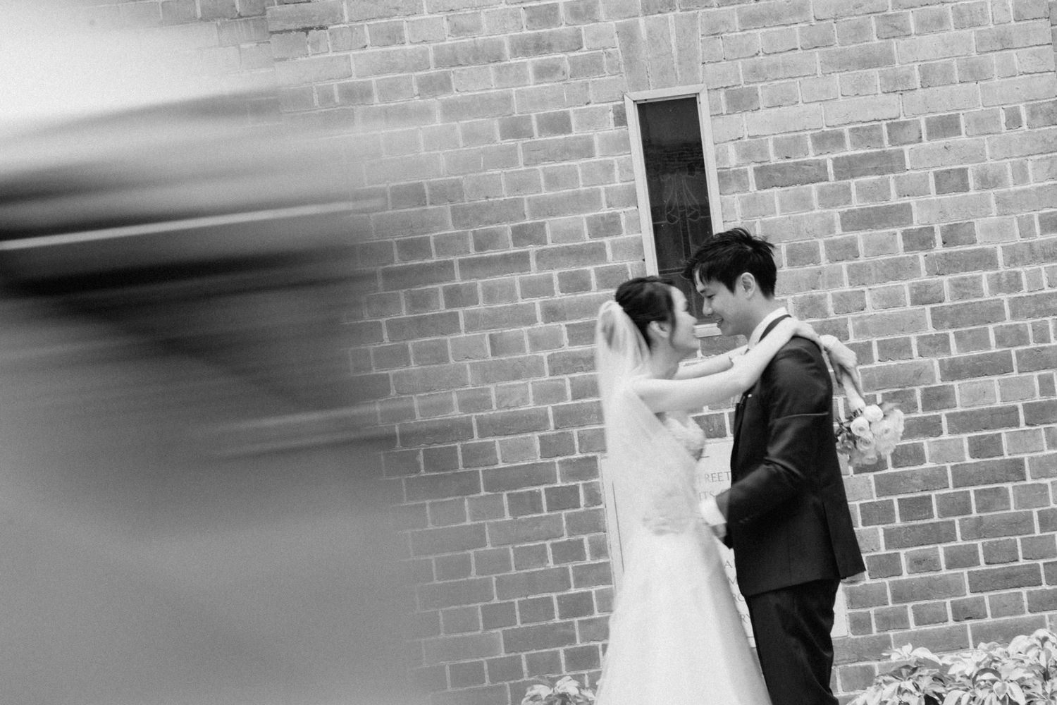 Artistic black and white shot of wedding couple against brick wall.