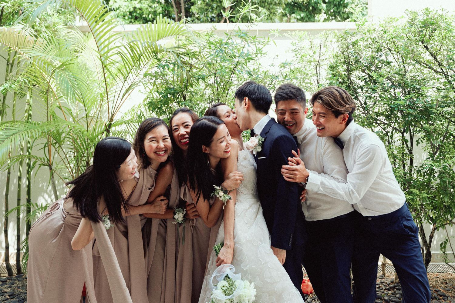 Wedding party shares candid moments in a garden with natural greenery backdrop.