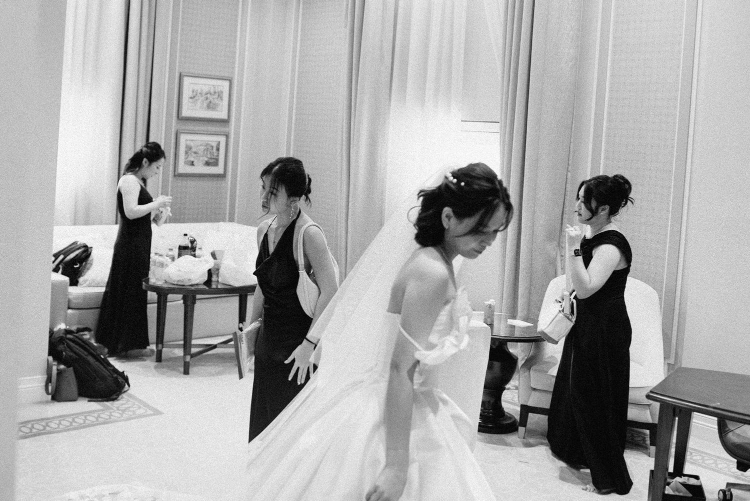 A bride in a white wedding gown gets ready with bridesmaids in black dresses in an elegant dressing room.