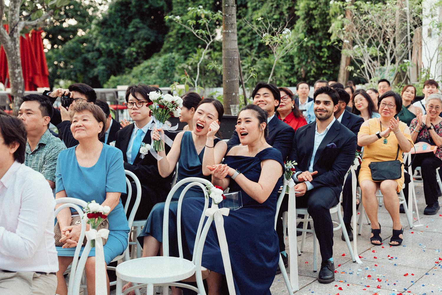 A crowd of people gathered outdoors in a park-like setting watching an event with trees in the background.