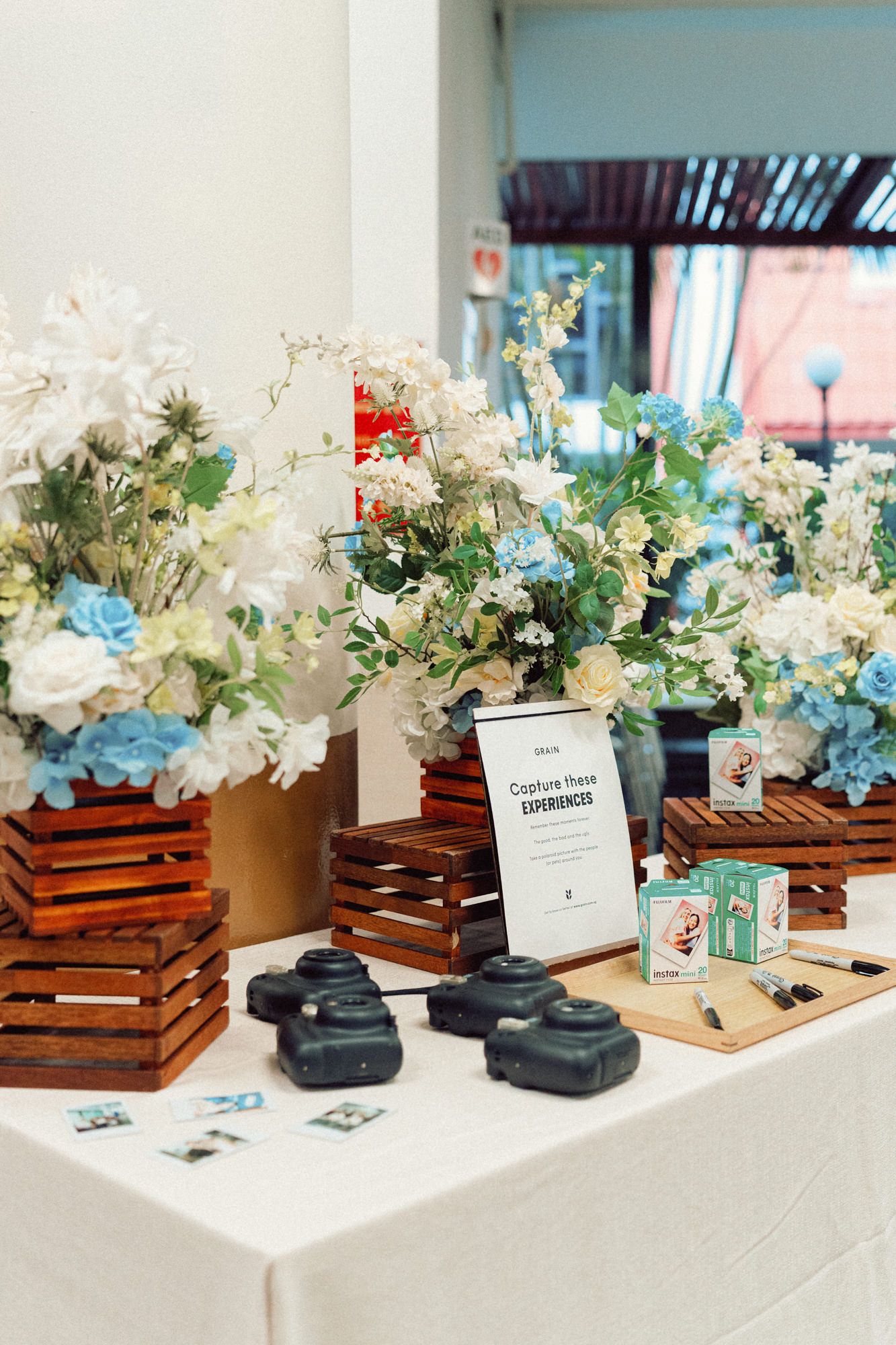 Wedding decorations featuring blue and white flowers in wooden crates with instant cameras on display.