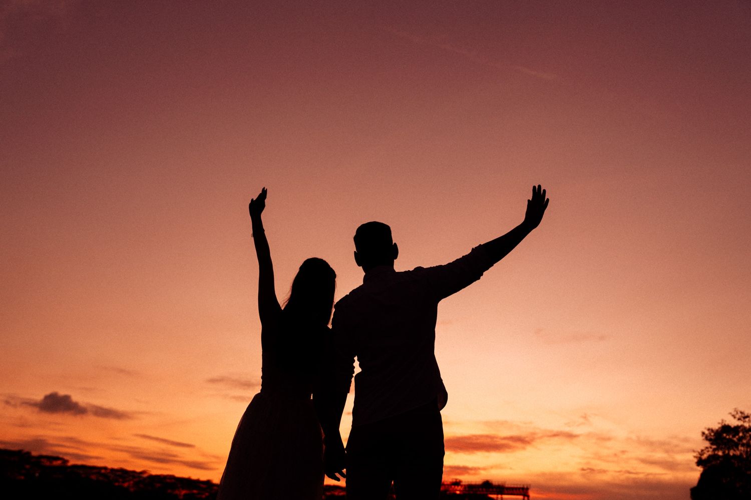 Silhouettes of people with raised arms against a dramatic orange sunset sky.