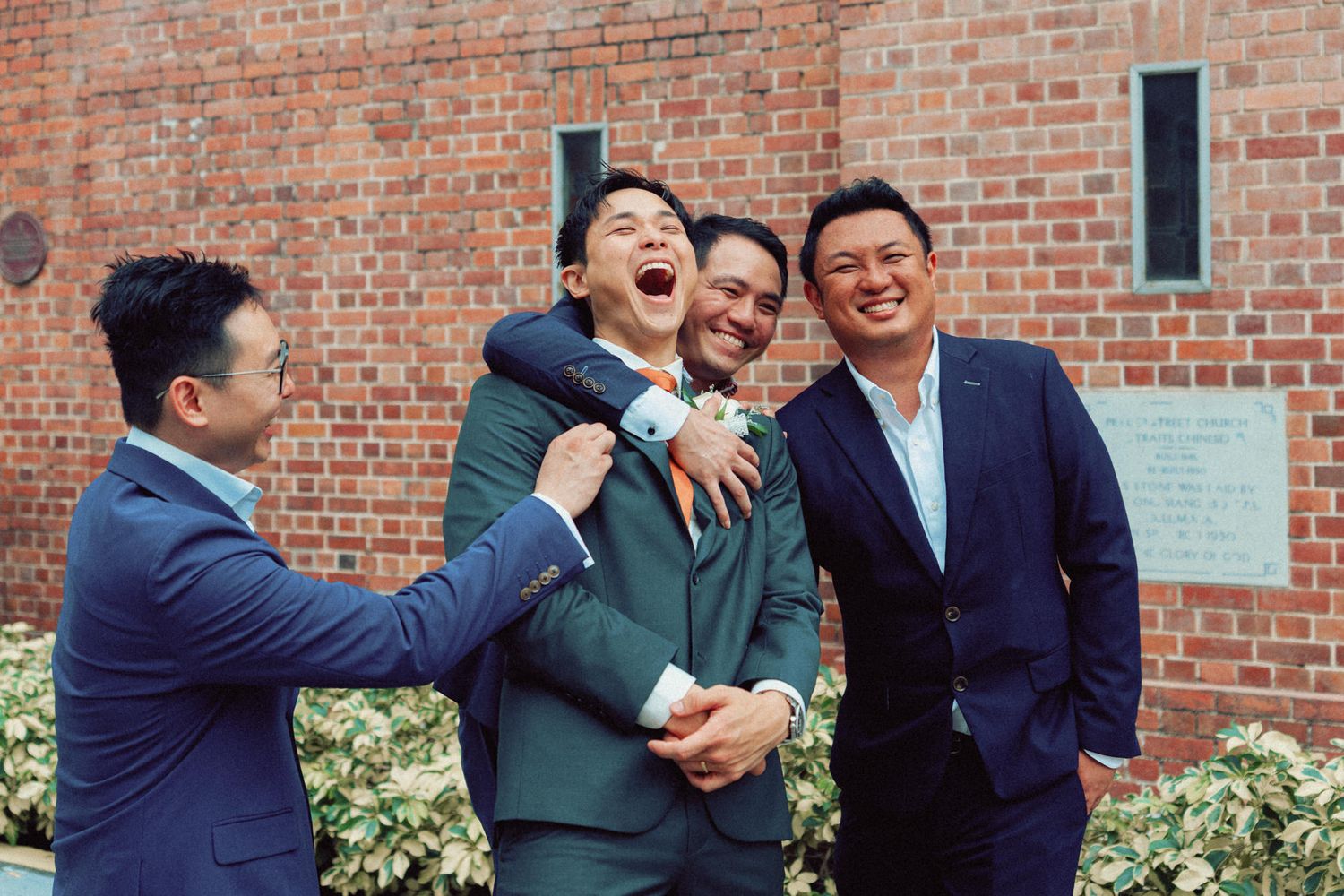 Groomsmen in suits sharing laughs outside brick church.