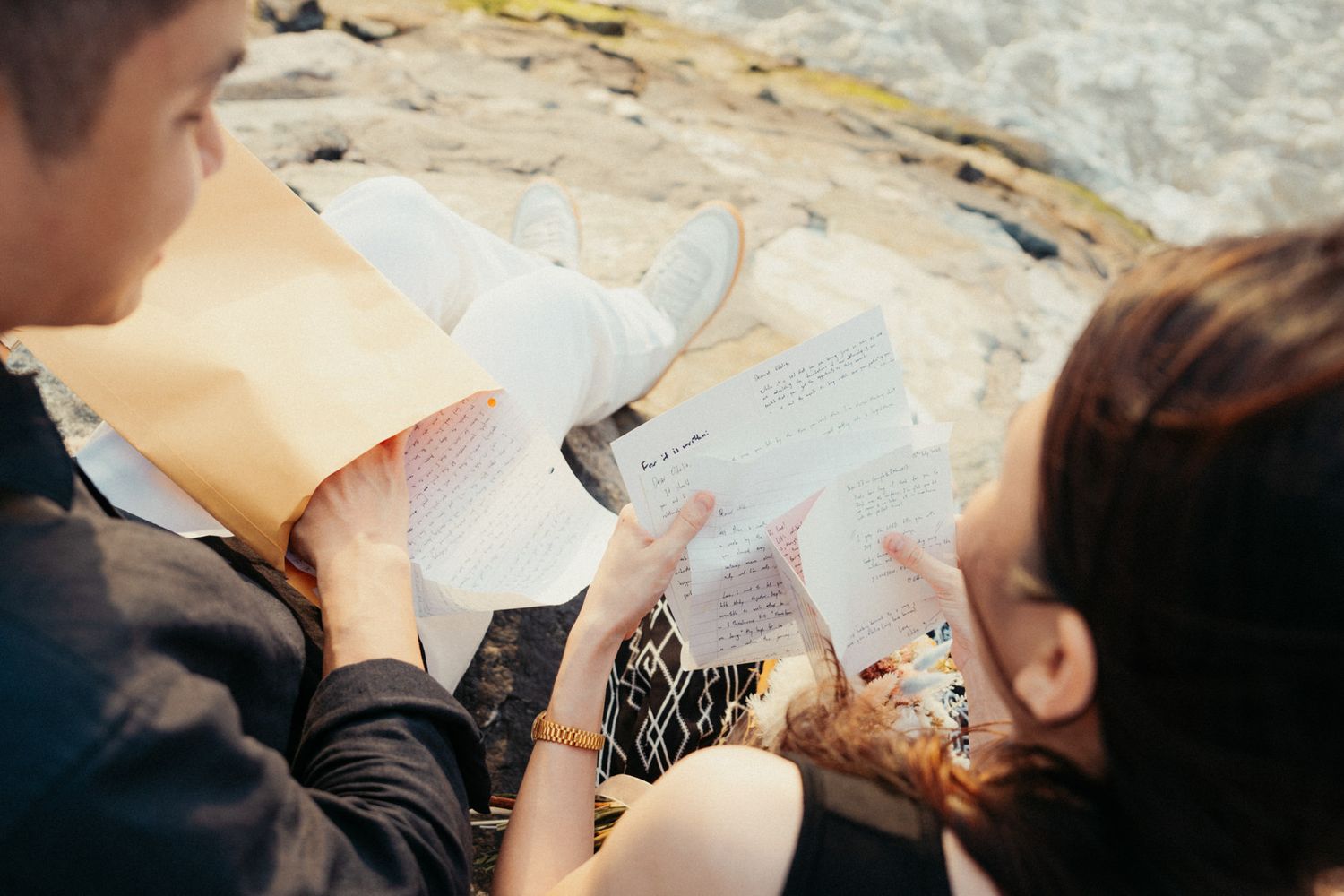 Two people relax together on rocky coastal formations by the sea.