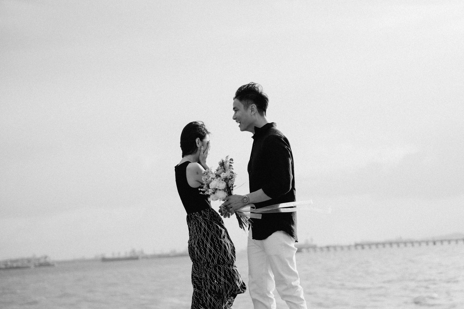 A romantic couple shares a tender moment at the beach with a bouquet of flowers.