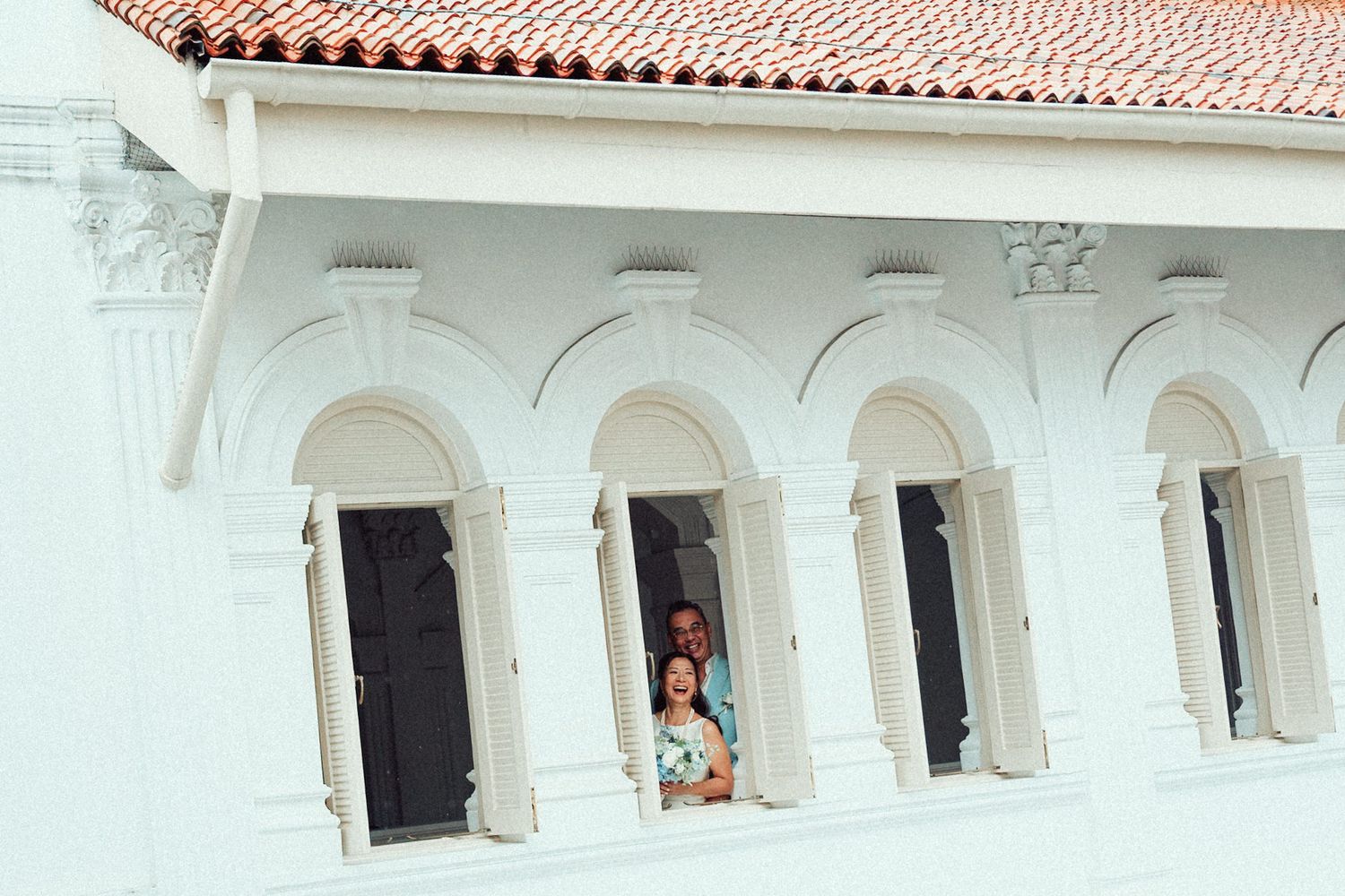 Spanish colonial building features terracotta roof tiles and white arched corridors with decorative columns.