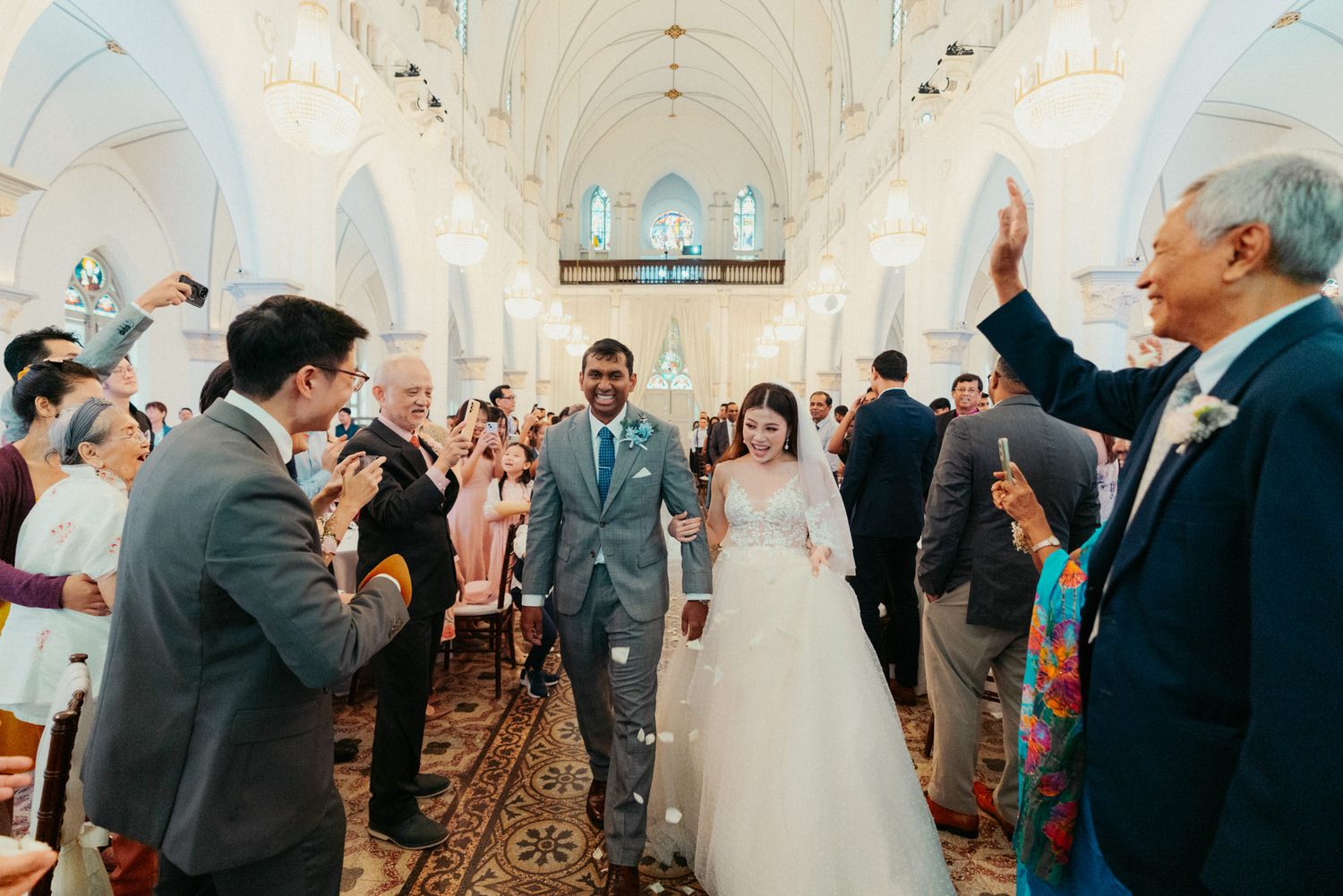 Newlywed couple walks down church aisle surrounded by cheering guests during joyful wedding ceremony.
