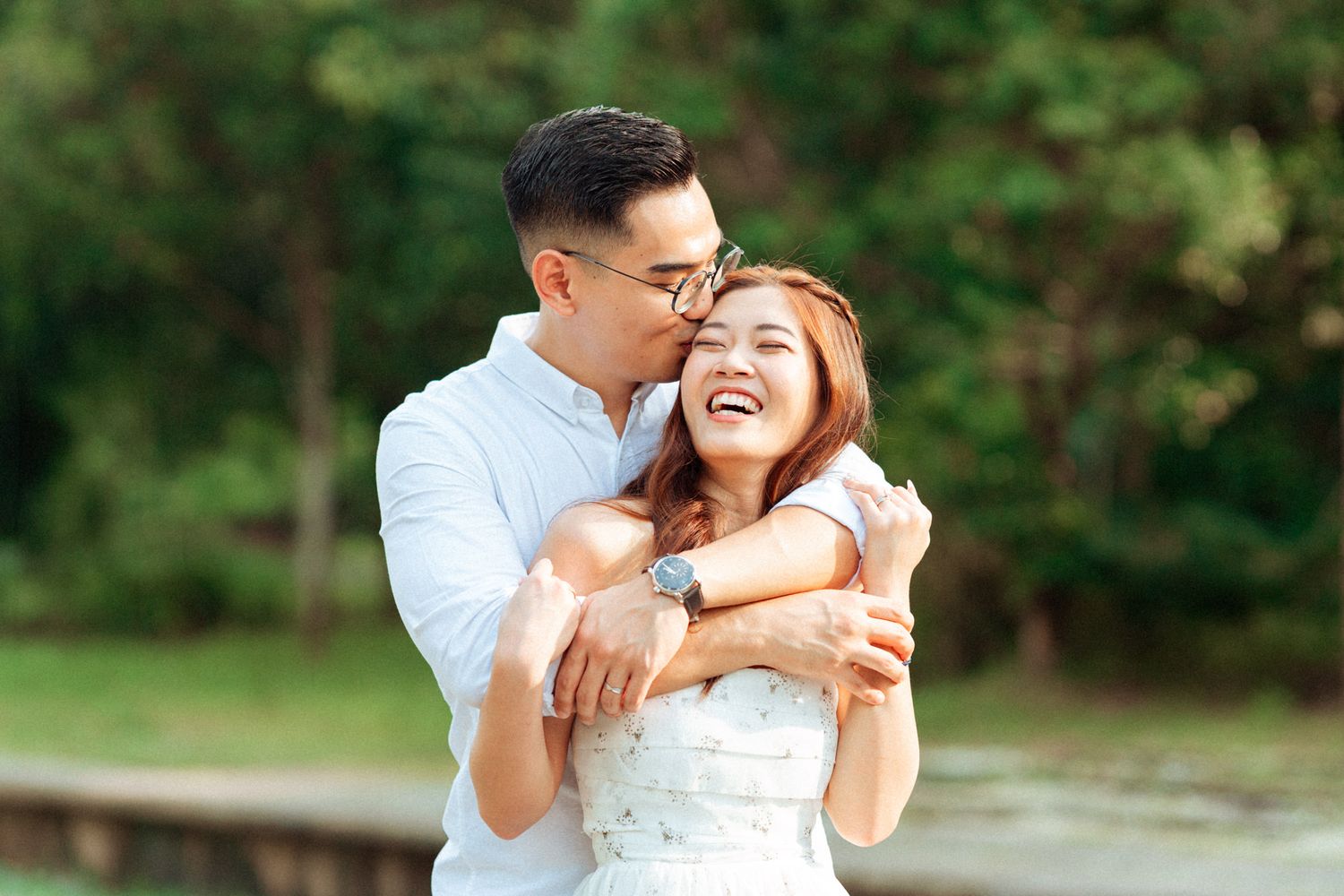 Couple shares joyful moment during outdoor photoshoot near trees.