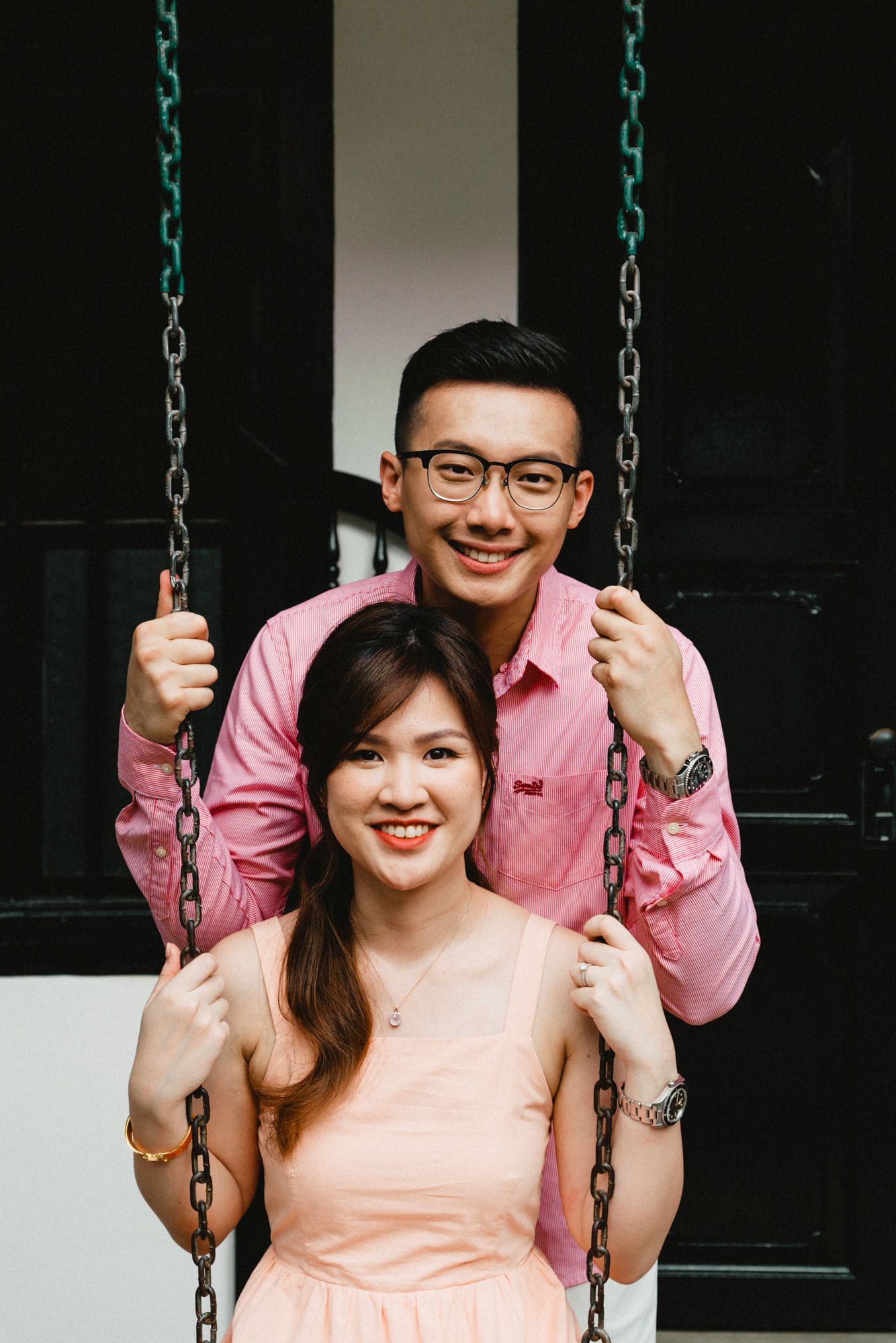 A couple enjoying a playful moment together on a swing set against a dark background.