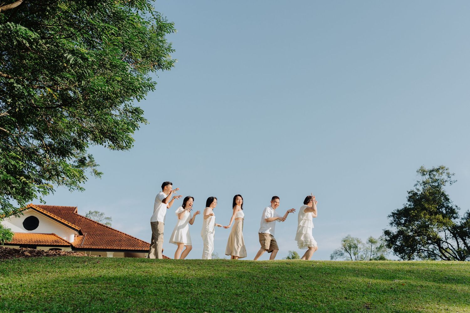 A group of people in white dresses walk along a grassy hilltop silhouetted against a blue summer sky.