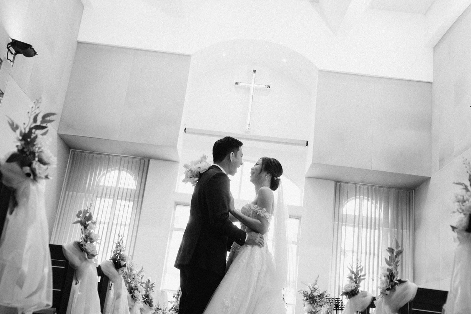 Black and white photo of a bride and groom sharing a romantic moment at a church wedding ceremony.