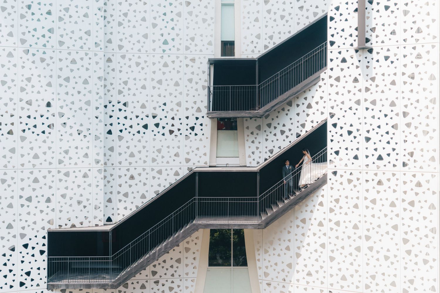 Person walking on modern black metal staircase against a white perforated geometric building facade.